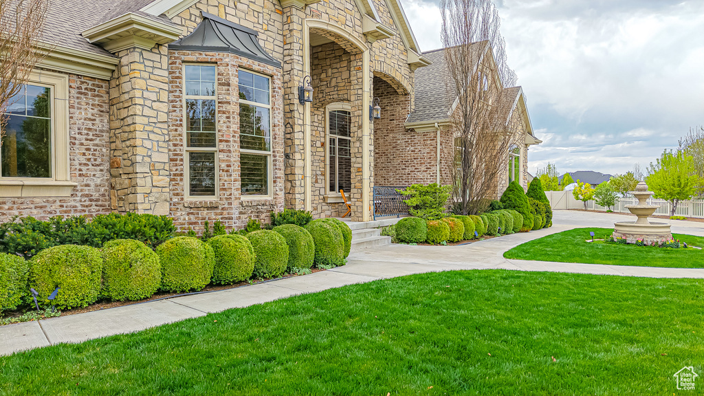 Property entrance featuring roof with shingles, fence, a yard, and brick siding