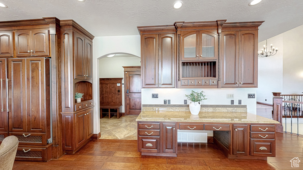 Kitchen with a textured ceiling, arched walkways, light stone counters, wood-type flooring, and glass insert cabinets