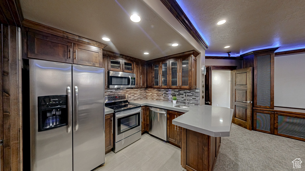 Kitchen with appliances with stainless steel finishes, a sink, light countertops, a peninsula, and recessed lighting