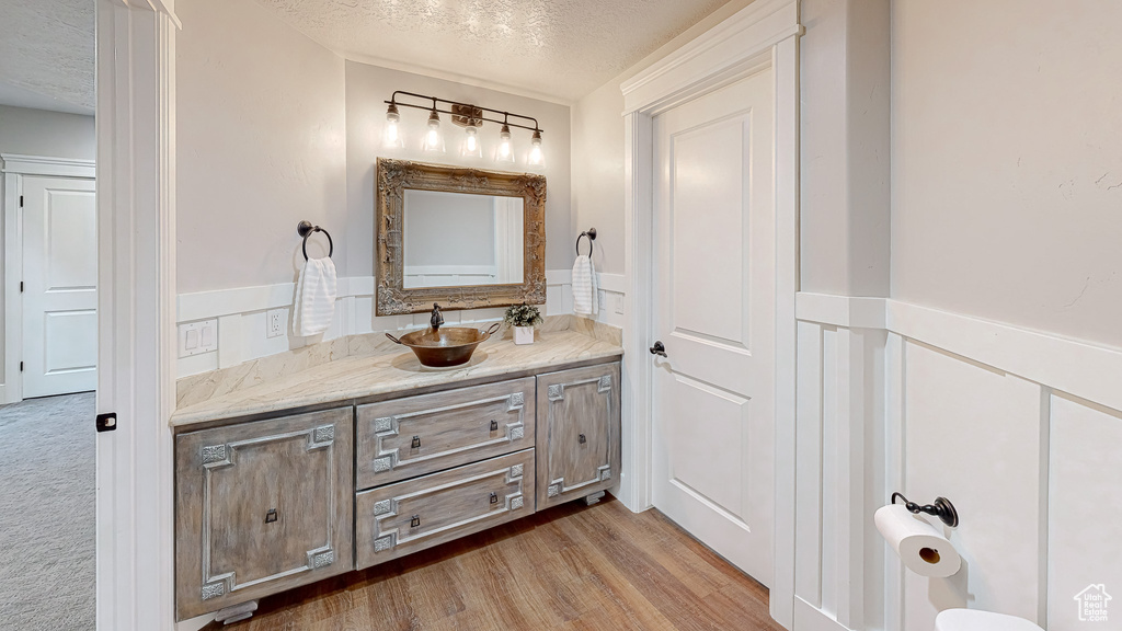 Bathroom with vanity, wainscoting, a textured ceiling, and wood finished floors
