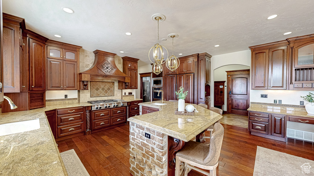 Kitchen featuring a sink, built in appliances, recessed lighting, custom range hood, and a kitchen bar