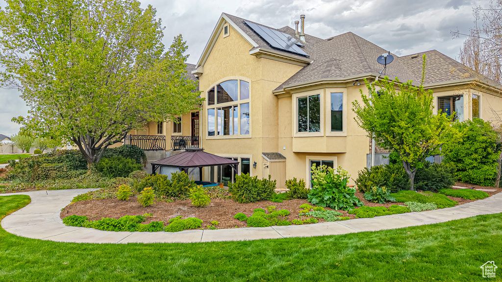Rear view of house with a gazebo, a lawn, stucco siding, and roof with shingles