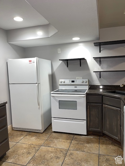 Kitchen featuring open shelves, dark brown cabinetry, dark countertops, white appliances, and a sink