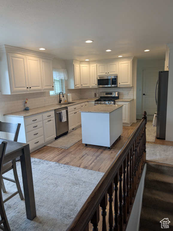 Kitchen featuring stainless steel appliances, a sink, light wood-style floors, decorative backsplash, and white cabinets