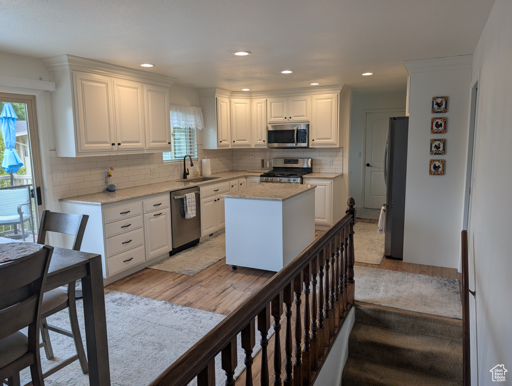 Kitchen with appliances with stainless steel finishes, a sink, light wood finished floors, white cabinets, and recessed lighting