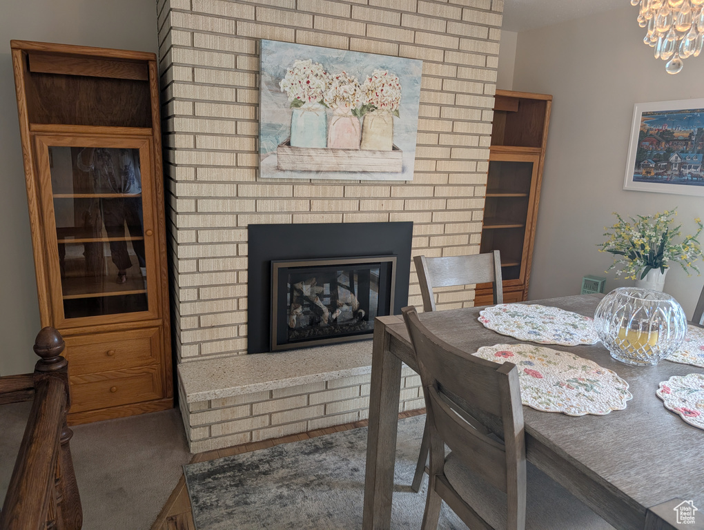 Carpeted dining space featuring a brick fireplace and a chandelier