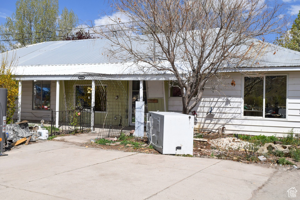 View of front of home featuring covered porch, gas water heater, ac unit, and metal roof
