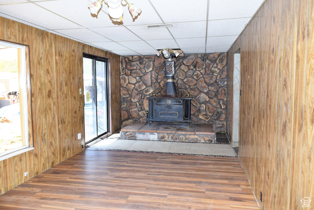 Unfurnished living room with wooden walls, a wood stove, a paneled ceiling, wood finished floors, and visible vents