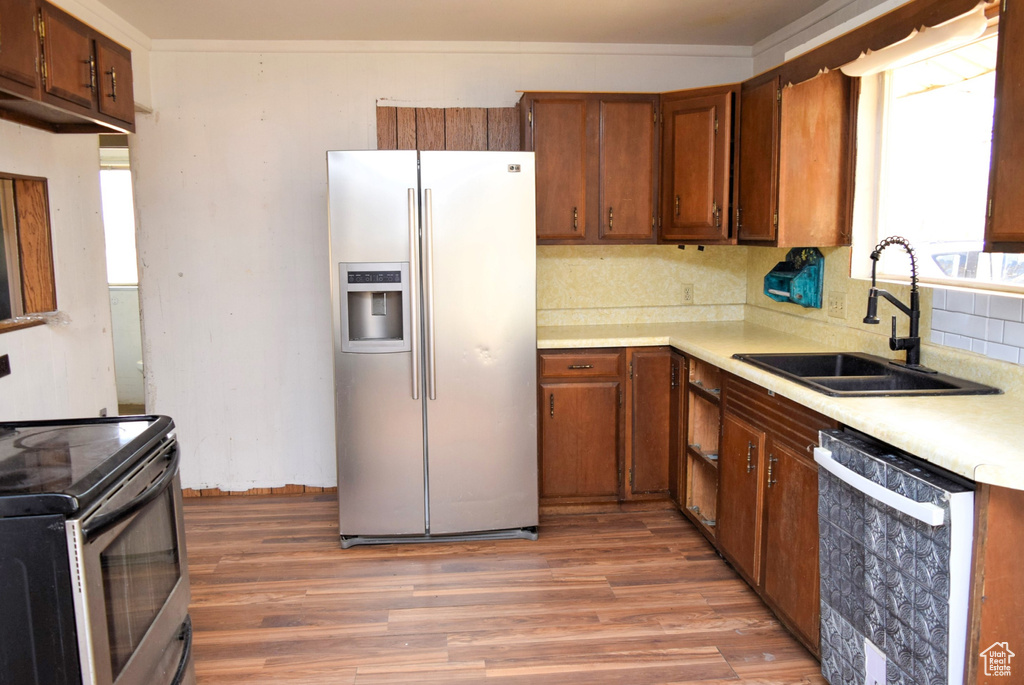 Kitchen with brown cabinets, a sink, light wood-style floors, light countertops, and stainless steel appliances