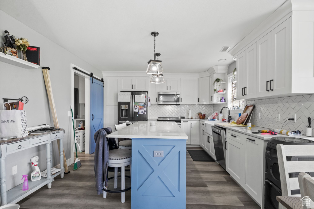 Kitchen with white cabinetry, open shelves, a barn door, stainless steel appliances, and a kitchen bar