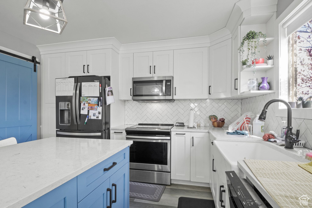 Kitchen featuring a barn door, stainless steel appliances, white cabinets, and backsplash