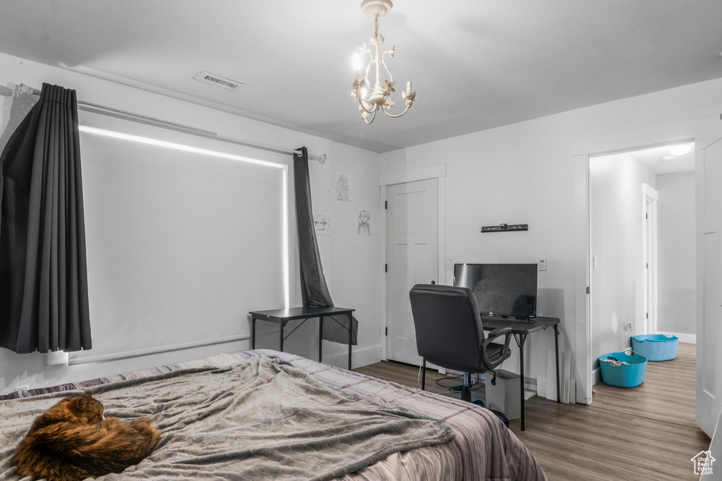 Bedroom with wood finished floors, visible vents, a chandelier, and baseboards