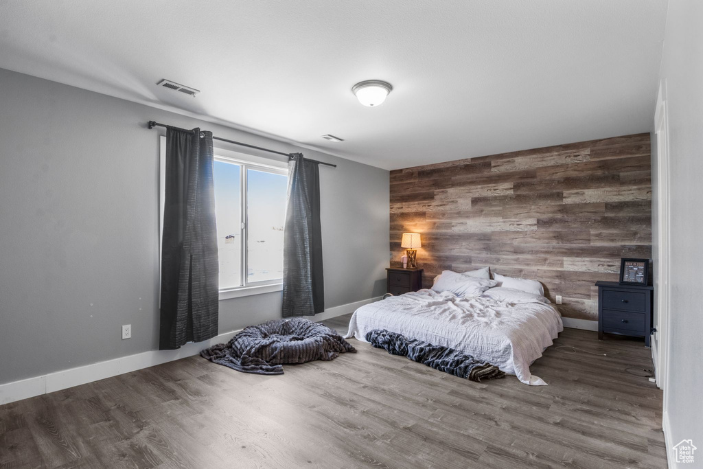 Bedroom with an accent wall, wooden walls, wood finished floors, and visible vents
