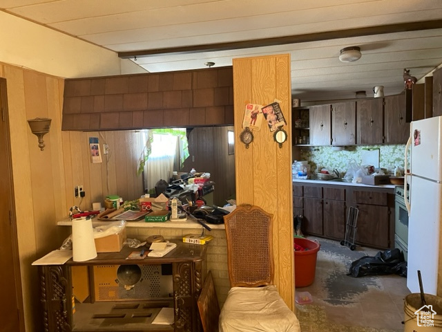Kitchen featuring dark brown cabinets, wooden walls, and white appliances