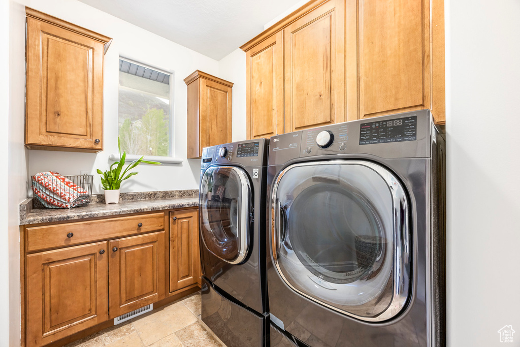 Laundry room with visible vents, stone finish flooring, cabinet space, and washing machine and clothes dryer