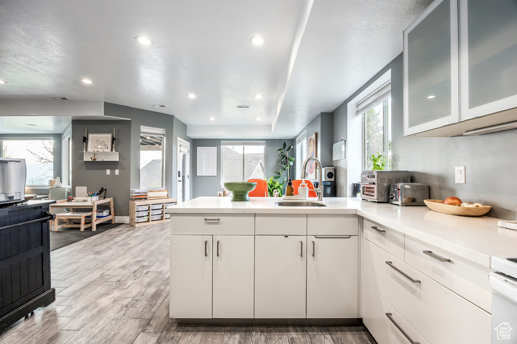 Kitchen with a peninsula, recessed lighting, light countertops, a sink, and light wood-style flooring
