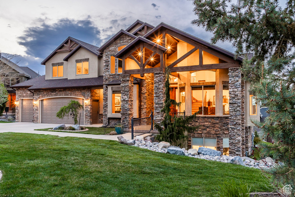 View of front of property featuring an attached garage, a front lawn, stone siding, stucco siding, and driveway