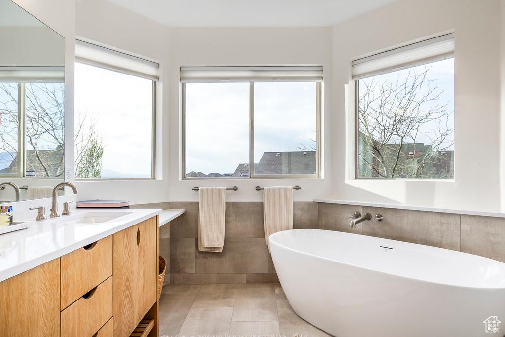 Bathroom featuring a freestanding tub, tile walls, a wealth of natural light, and vanity