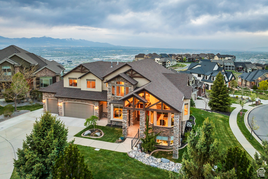 View of front facade featuring driveway, a front yard, a shingled roof, stone siding, and stucco siding