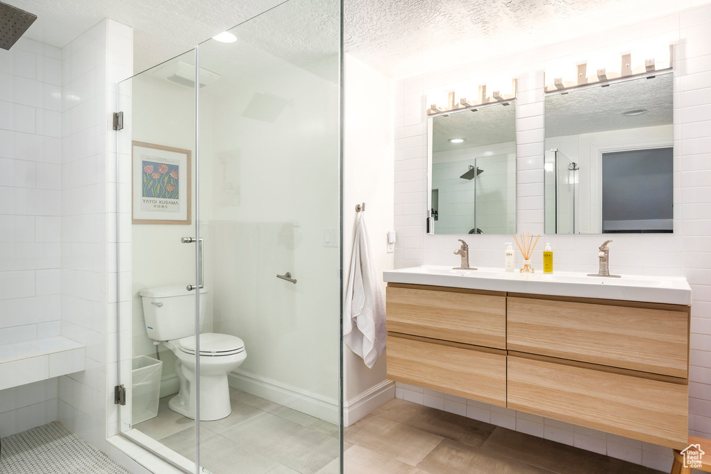 Bathroom featuring double vanity, a textured ceiling, a stall shower, and toilet