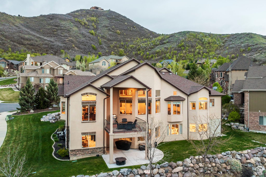 Rear view of property featuring a lawn, a patio, stucco siding, and a balcony