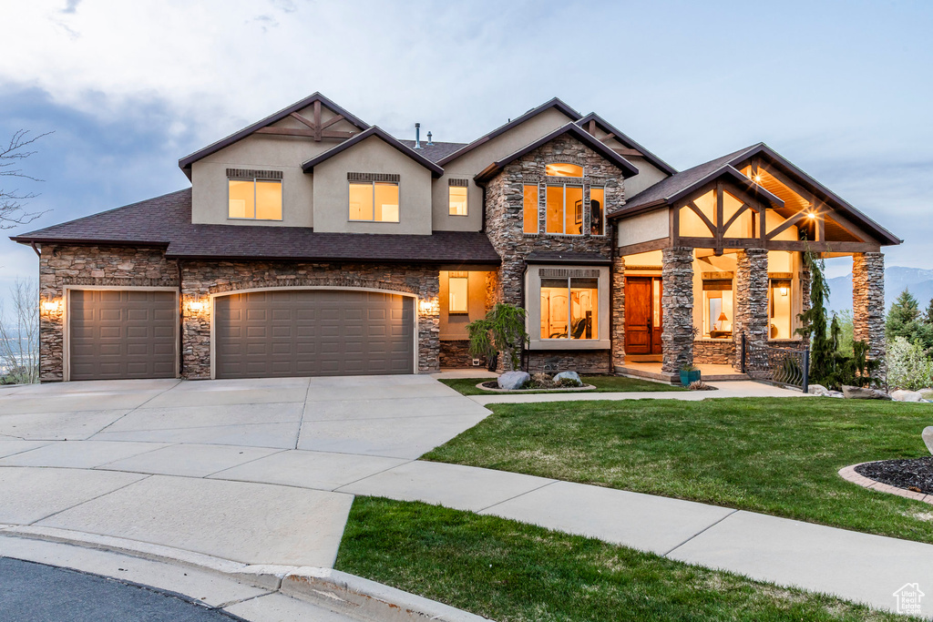 Craftsman house featuring a garage, a front lawn, stone siding, stucco siding, and driveway