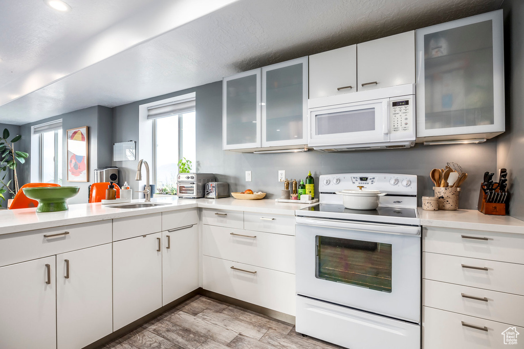 Kitchen with white appliances, white cabinets, a sink, and light countertops