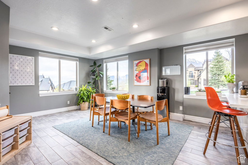 Dining space with plenty of natural light, a tray ceiling, light wood finished floors, and visible vents