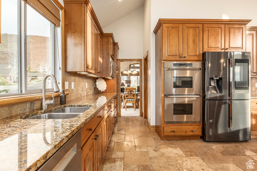Kitchen with stone tile flooring, brown cabinetry, tasteful backsplash, a sink, and stainless steel appliances