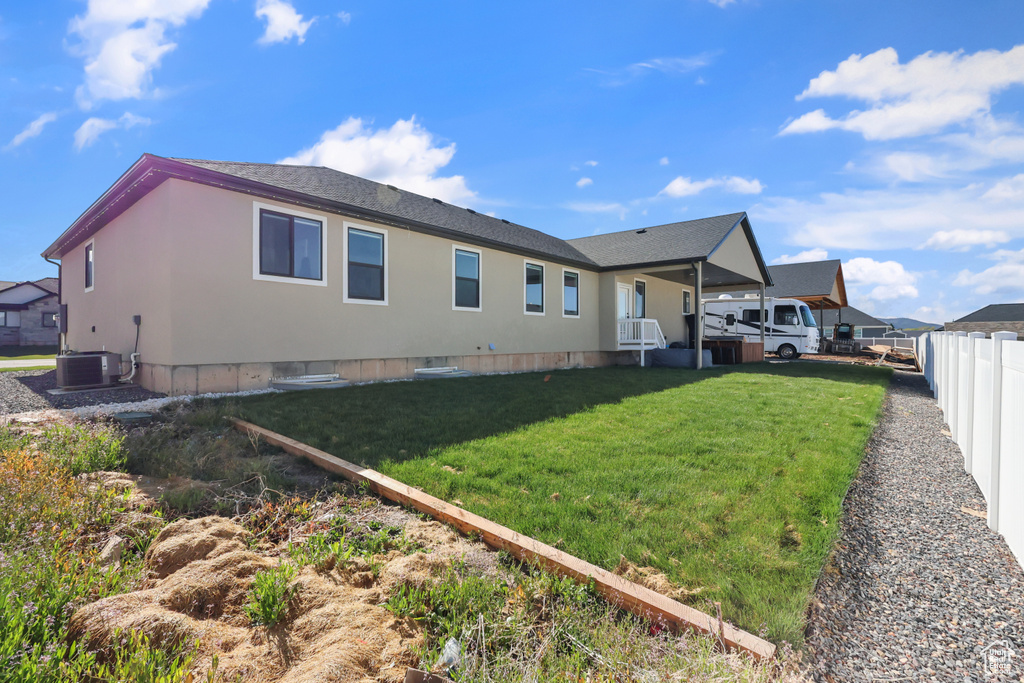 Rear view of house with fence, central AC unit, a lawn, and roof with shingles