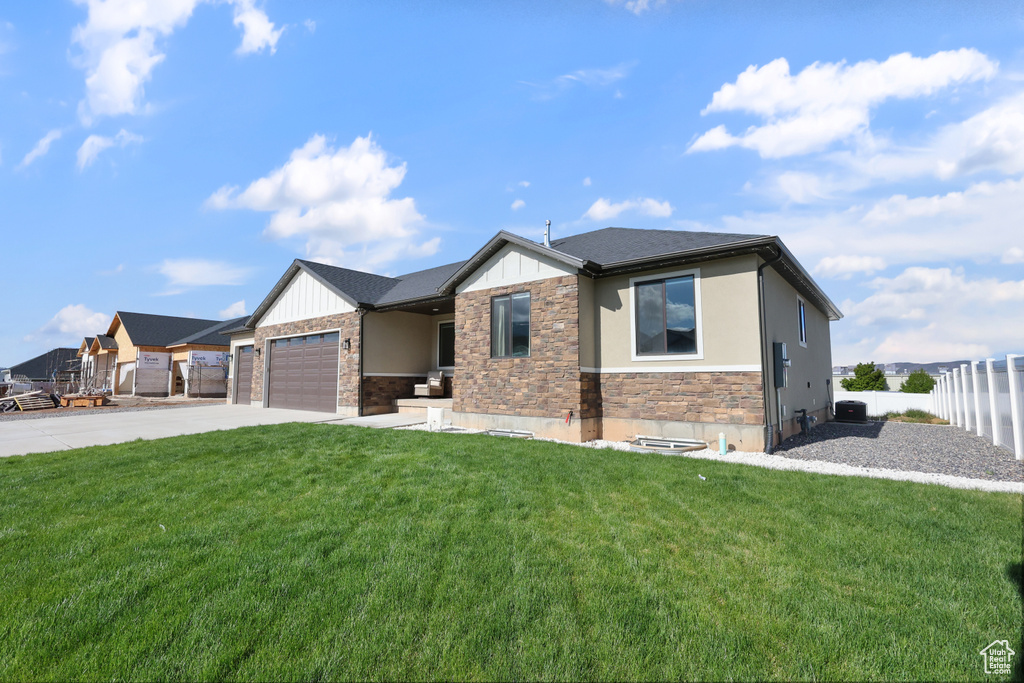 Prairie-style house featuring a garage, fence, a front lawn, concrete driveway, and stone siding
