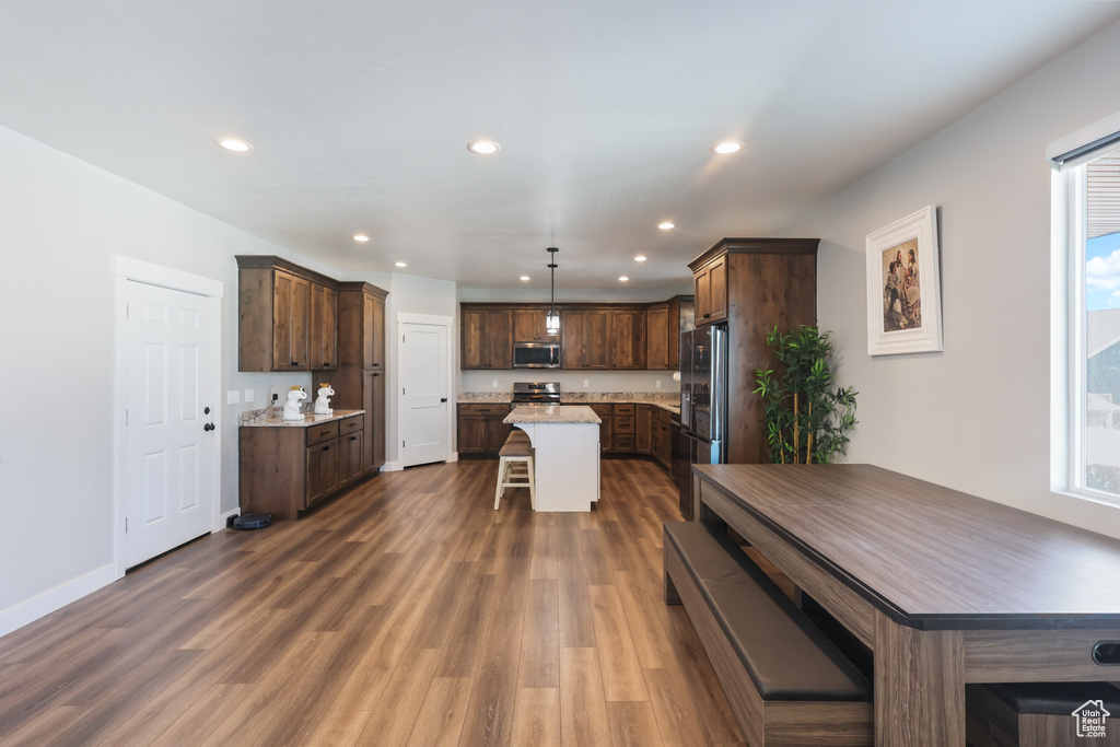 Kitchen with dark wood-style flooring, a kitchen island, a kitchen breakfast bar, recessed lighting, and stainless steel appliances
