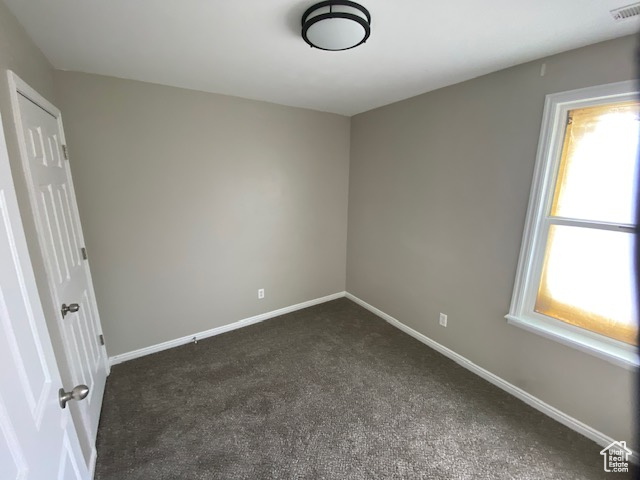 Empty room featuring visible vents, dark carpet, and baseboards