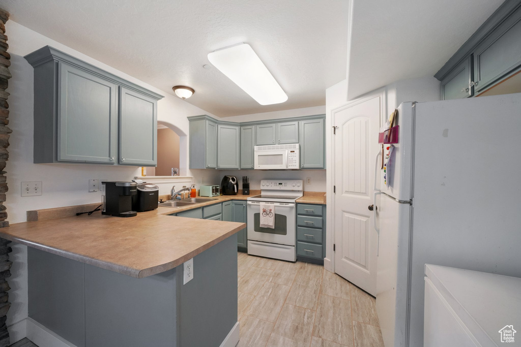 Kitchen featuring a sink, white appliances, arched walkways, a peninsula, and gray cabinetry