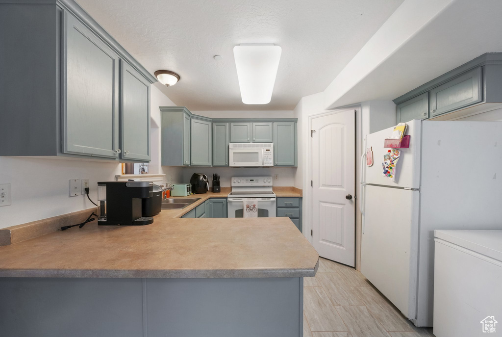 Kitchen with light countertops, gray cabinetry, a sink, a peninsula, and white appliances