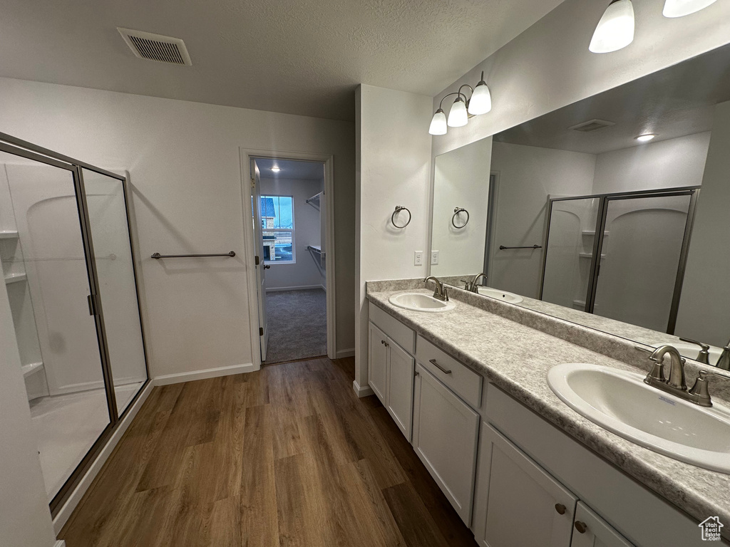 Bathroom featuring wood finished floors, a stall shower, double vanity, a textured ceiling, and baseboards