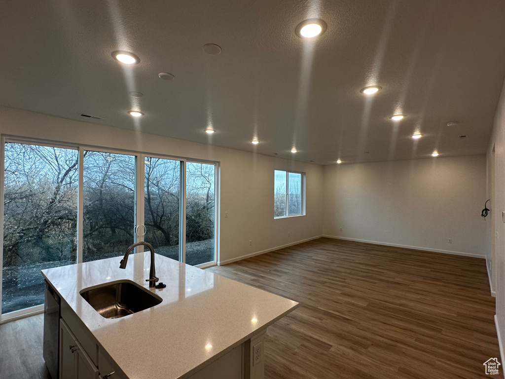 Kitchen featuring a sink, wood finished floors, baseboards, open floor plan, and light stone countertops