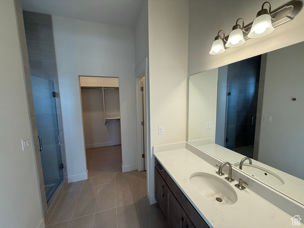 Bathroom with tile patterned floors, a shower stall, a walk in closet, and vanity
