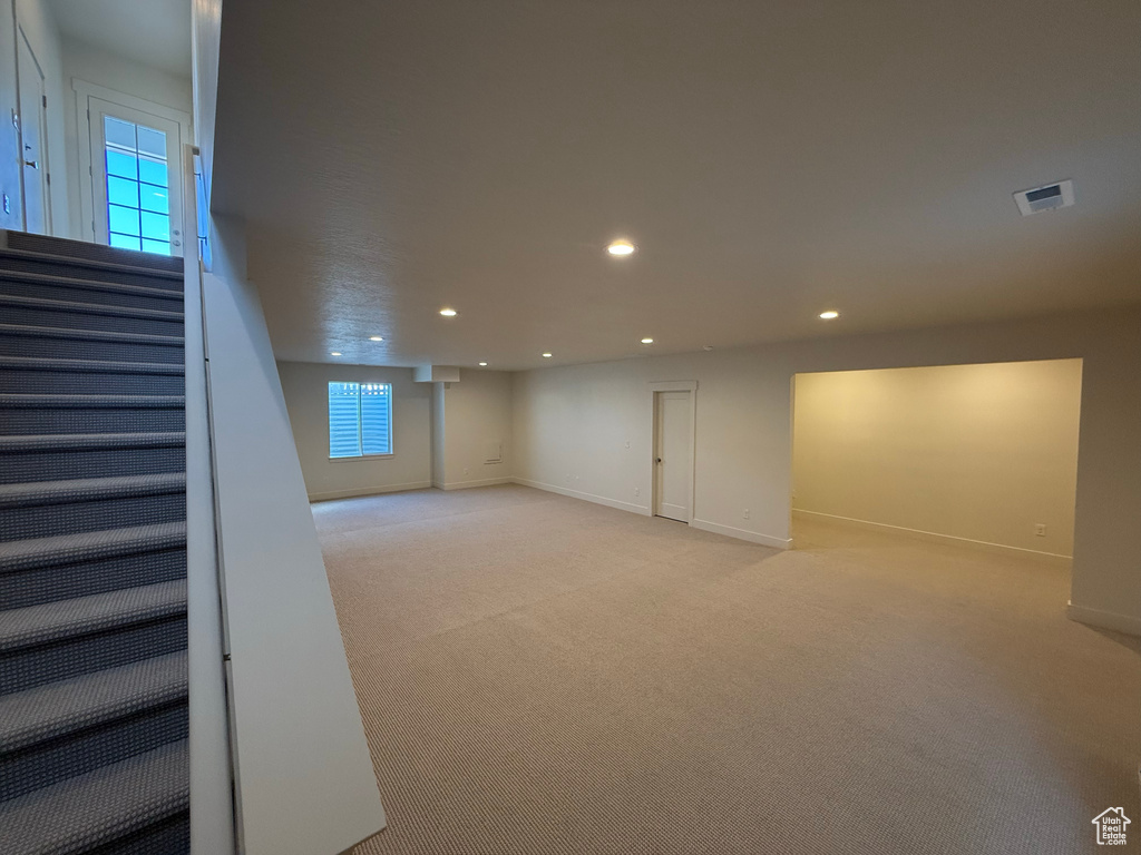 Below grade area with light colored carpet, visible vents, stairs, baseboards, and recessed lighting