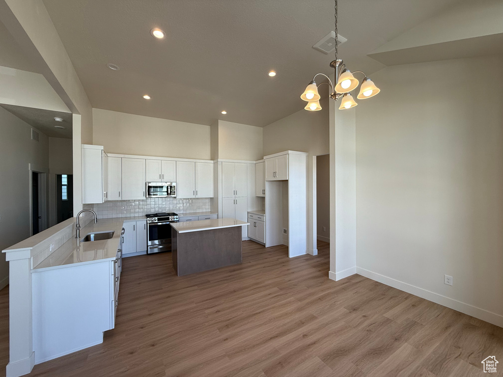 Kitchen with a kitchen island, appliances with stainless steel finishes, tasteful backsplash, a sink, and high vaulted ceiling