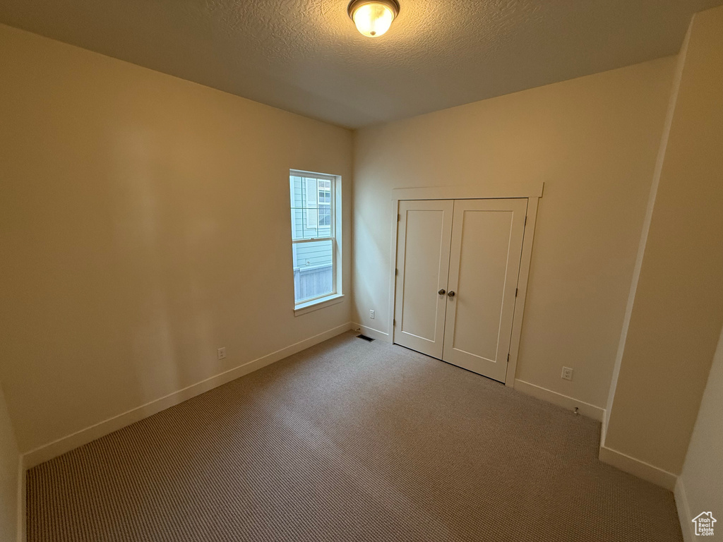 Carpeted spare room with baseboards, a textured ceiling, and visible vents