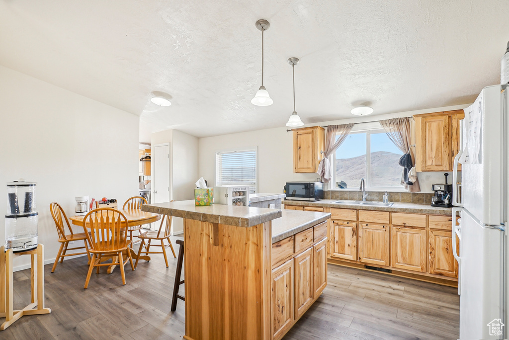 Kitchen with black microwave, a sink, freestanding refrigerator, light brown cabinets, and light wood-style flooring