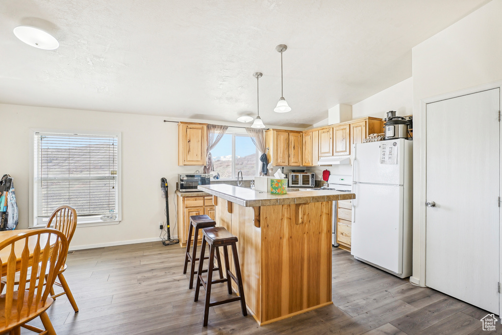Kitchen with freestanding refrigerator, range with electric cooktop, a kitchen island, and light brown cabinets