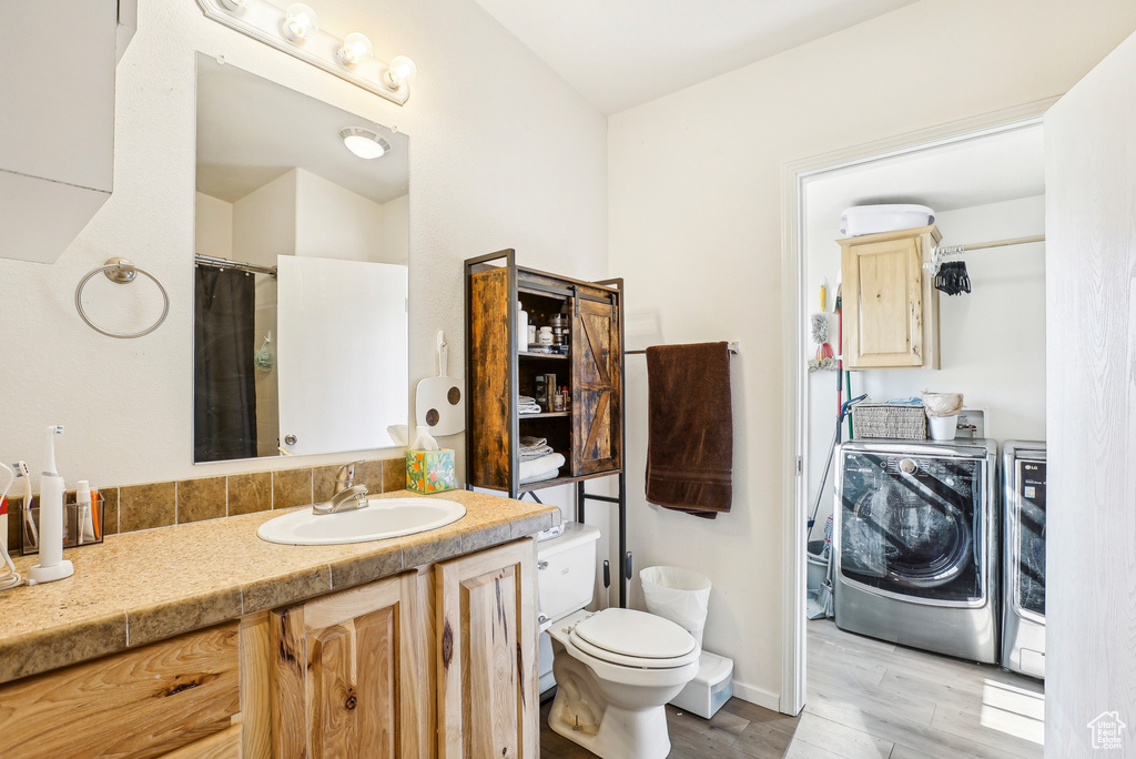 Bathroom featuring washer and dryer, vanity, toilet, wood finished floors, and wine cooler