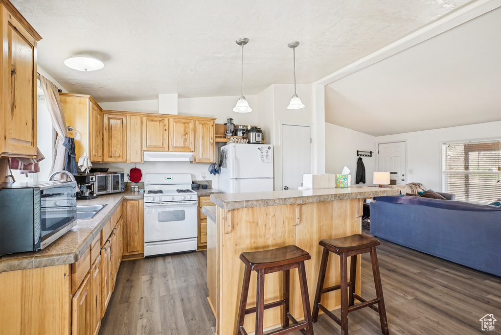 Kitchen with vaulted ceiling, wood finished floors, a breakfast bar, under cabinet range hood, and white appliances