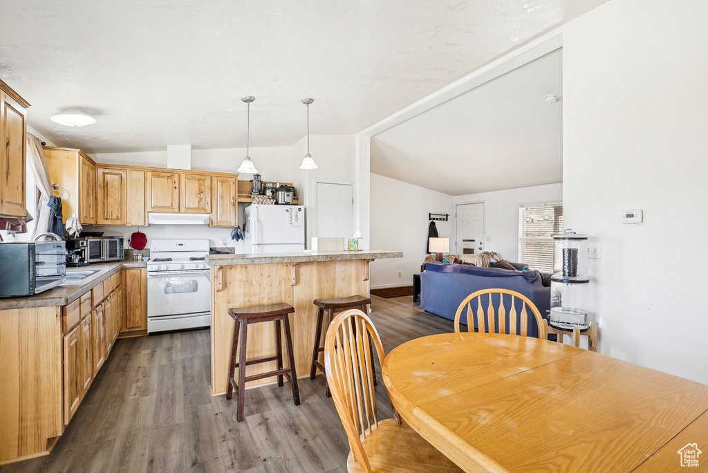 Kitchen with lofted ceiling, a kitchen island, white appliances, dark wood-type flooring, and under cabinet range hood
