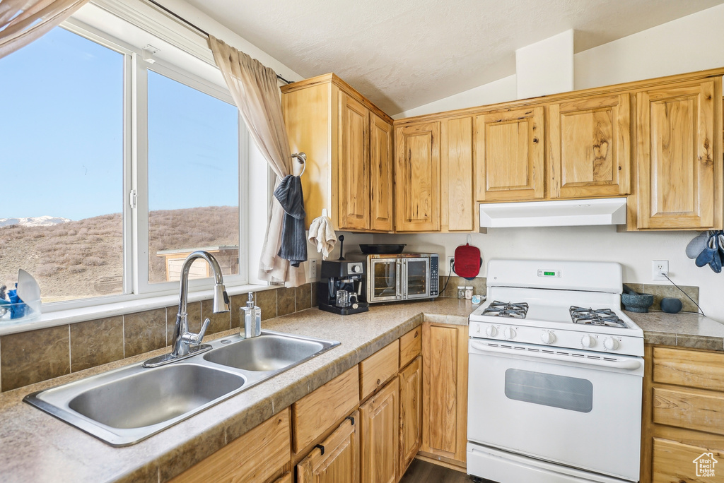 Kitchen featuring a toaster, white gas range, under cabinet range hood, a sink, and vaulted ceiling