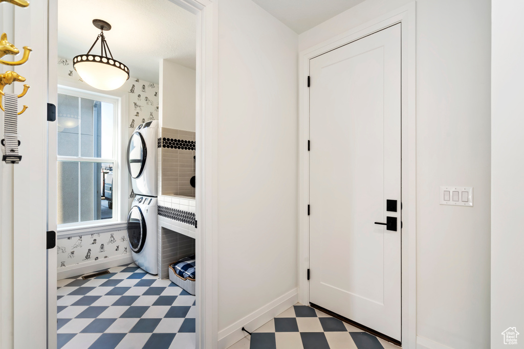 Clothes washing area featuring laundry area, light floors, stacked washing maching and dryer, and baseboards