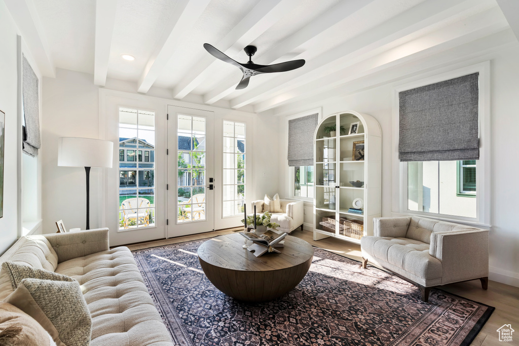 Living room with a ceiling fan, plenty of natural light, beam ceiling, and wood finished floors