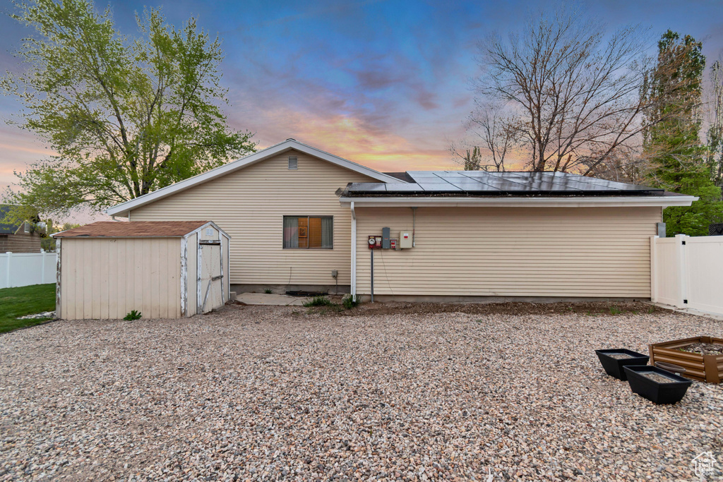 Back of house at dusk featuring roof mounted solar panels, fence, an outdoor structure, and a shed
